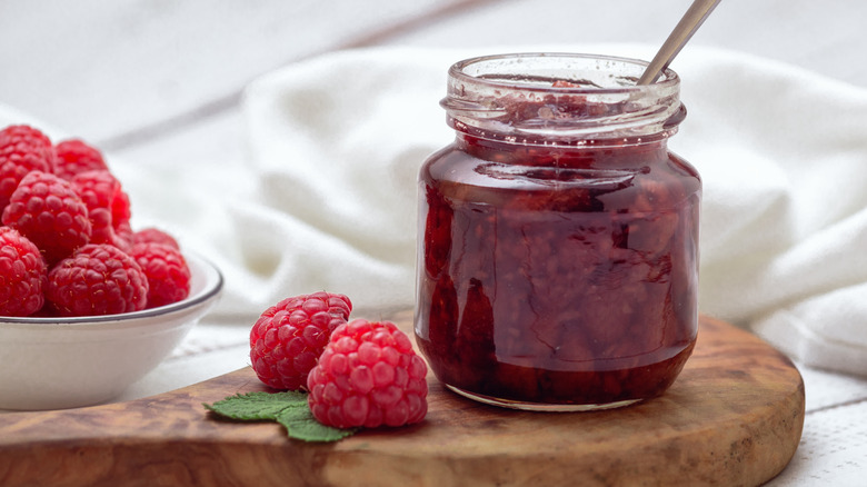 jar of raspberry jam on a cutting board with fresh raspberries