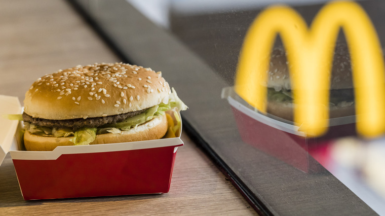 A McDonald's big mac next to a window with the McDonald's sign in the reflection