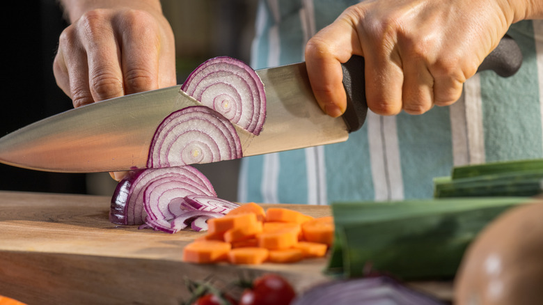 Hands chop red onion on a wood cutting board