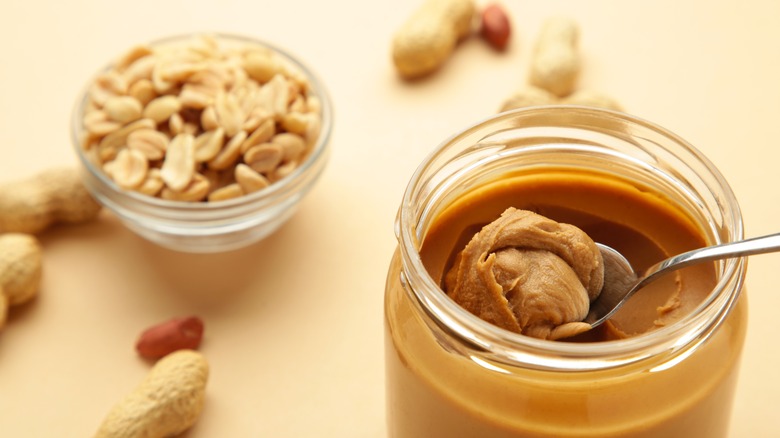 jar of peanut butter beside bowl of peanuts