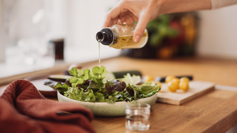 person pouring dressing on salad