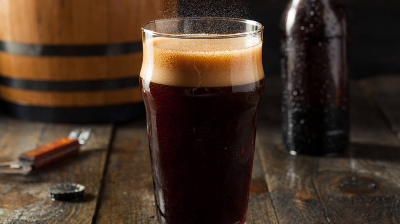 A glass of fizzling root beer beside a brown bottle and bottle opener