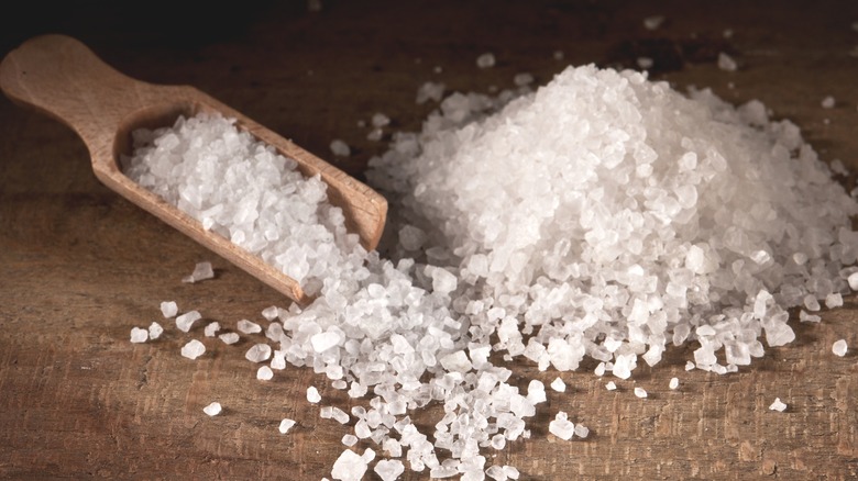 A pile of coarse-grained salt with wooden scoop.