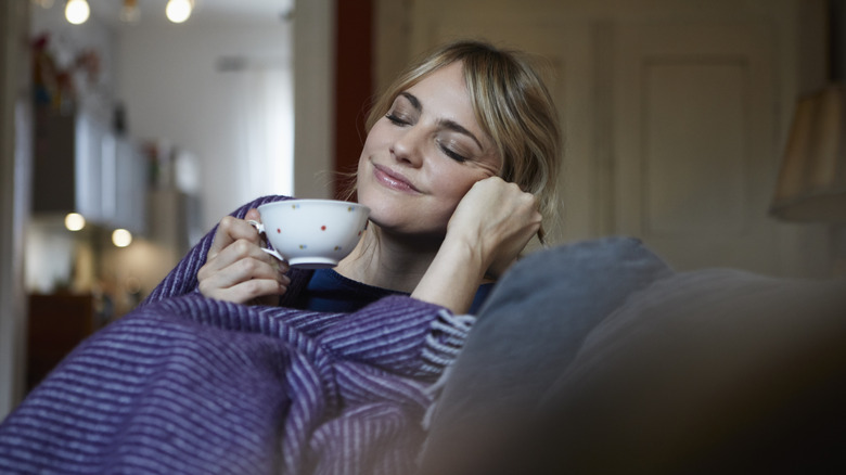 A person relaxing on a sofa holding a cup of tea