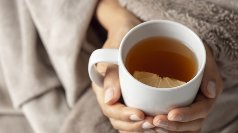 Person wrapped in a blanket holding a cup of tea with a lemon slice in it