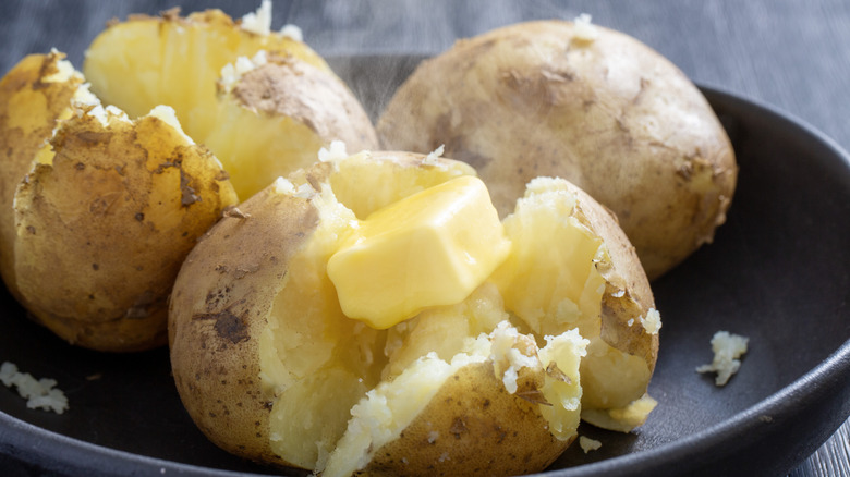 Plate of steaming hot baked potatoes, one topped with a butter pat