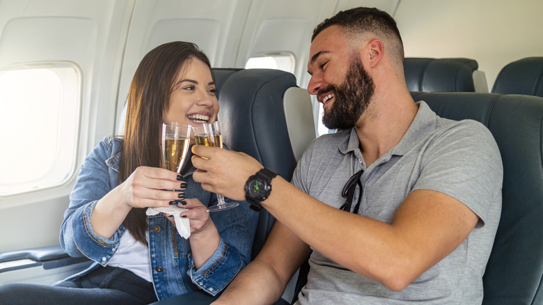 happy couple toasting glasses of champagne in airplane seats