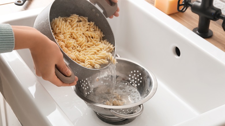 Hands draining pasta and water into colander in sink