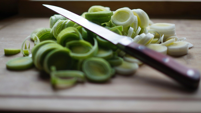 A cutting board with chopped leeks and a knife