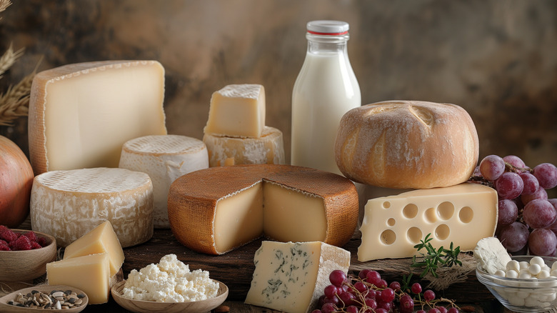 Various types of cheese with fruits and milk on a wooden table.