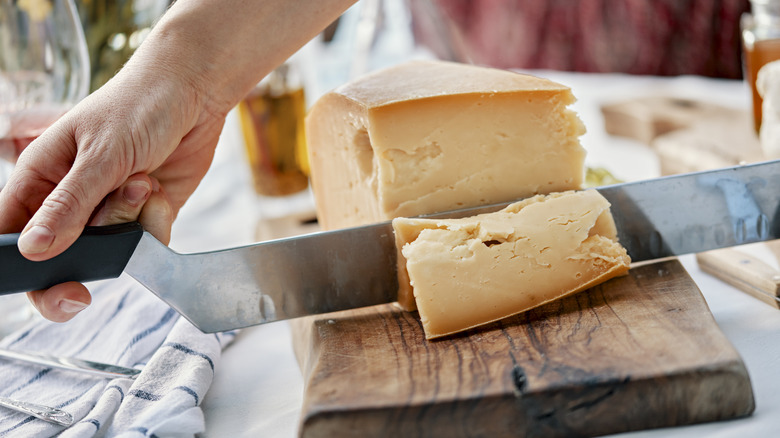 A person cutting cheese on a wooden chopping board.