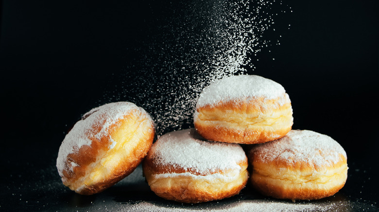 Powdered sugar being sprinkled onto four donuts