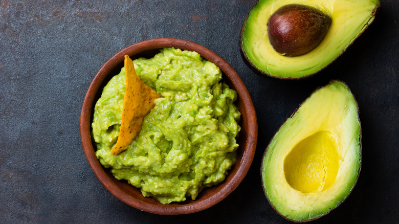 A bowl of guacamole and two avocados