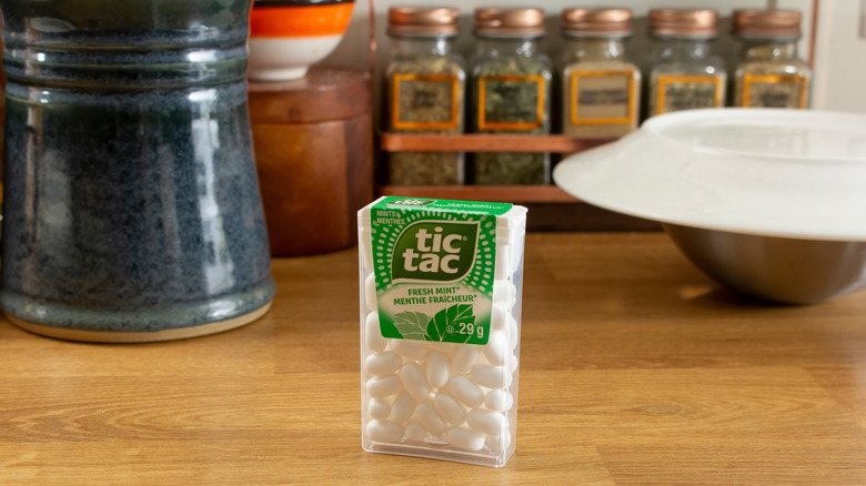 A white pack of Tic Tacs in front of a few spice jars and other kitchen items