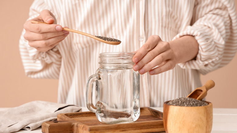 A person spooning seeds into a mason jar