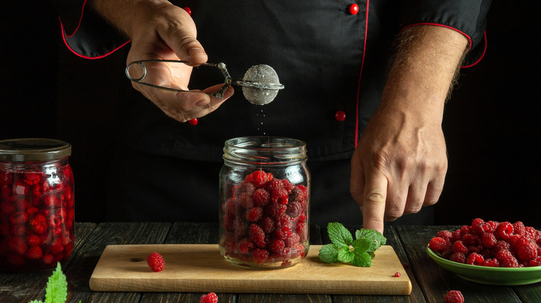 Person sprinkling sugar on jar of raspberries