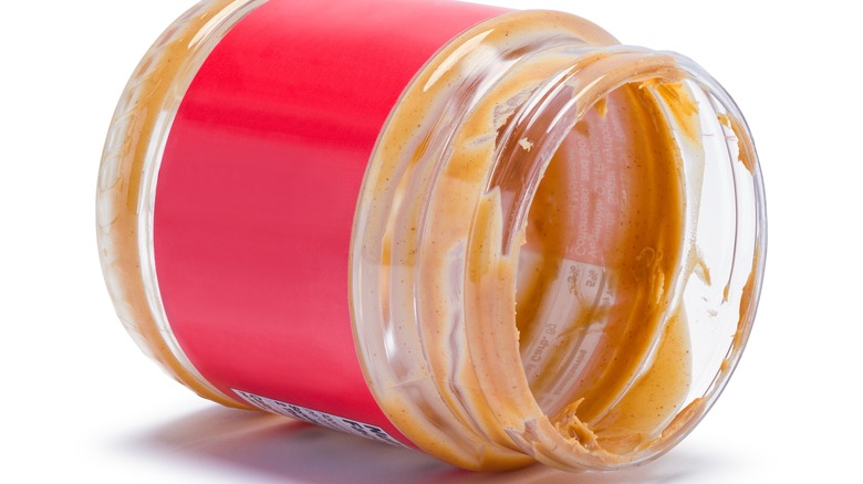 An empty jar of peanut butter on its side on a white background