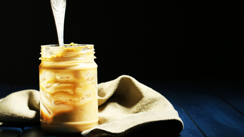 A mostly empty jar of peanut butter with a spoon in it on a dark background