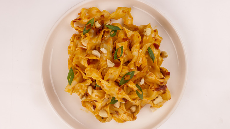 Peanut noodles with green onions and peanuts on a white plate