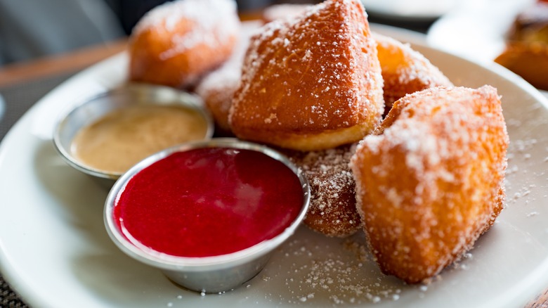 beignets on plate with small cups of dipping sauces