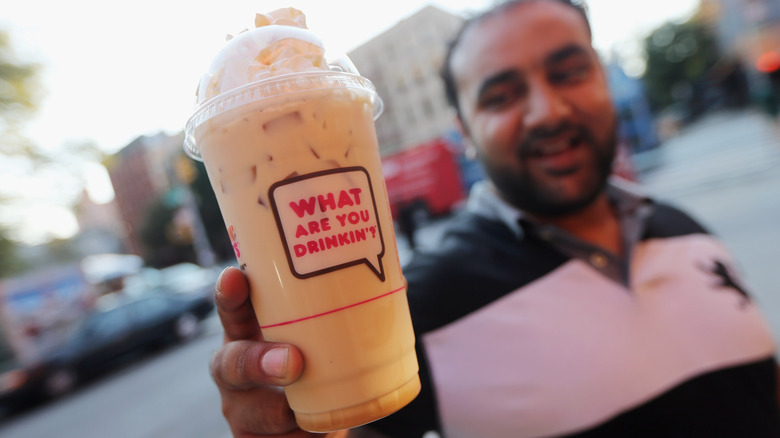 Person holding banana-flavored iced Dunkin' drink with whipped cream