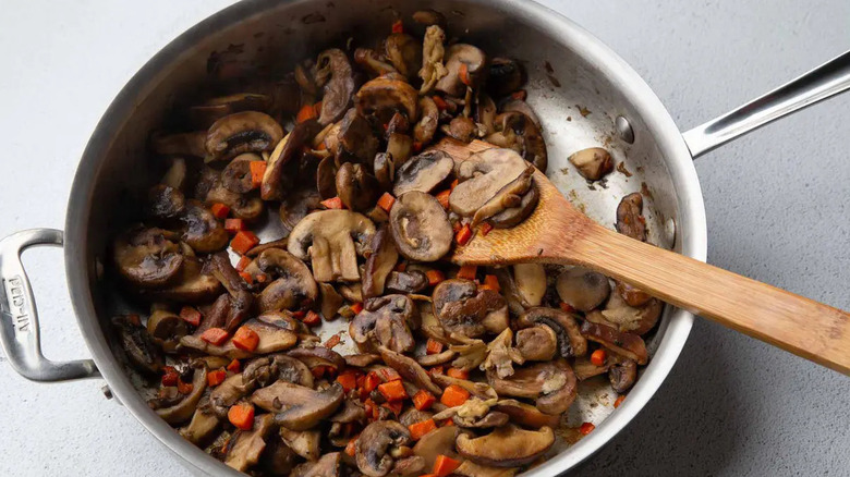 Mushrooms and carrots in skillet with wooden spatula