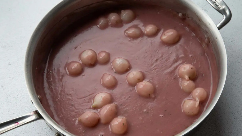 Reddish gravy in skillet with pearl onions