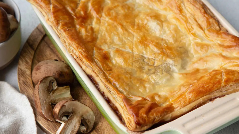 Golden pastry on baking dish next to sliced mushrooms