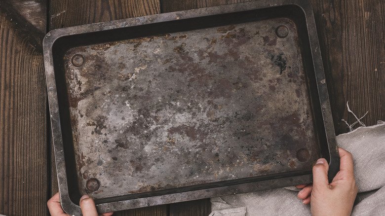 A person holding a dirty baking sheet