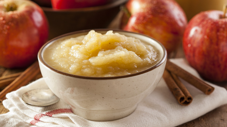 Applesauce bowl on towel by apples and cinnamon sticks