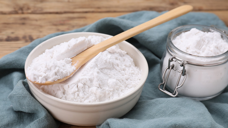 Cornstarch and spoon in wooden bowl by jar and blue towel