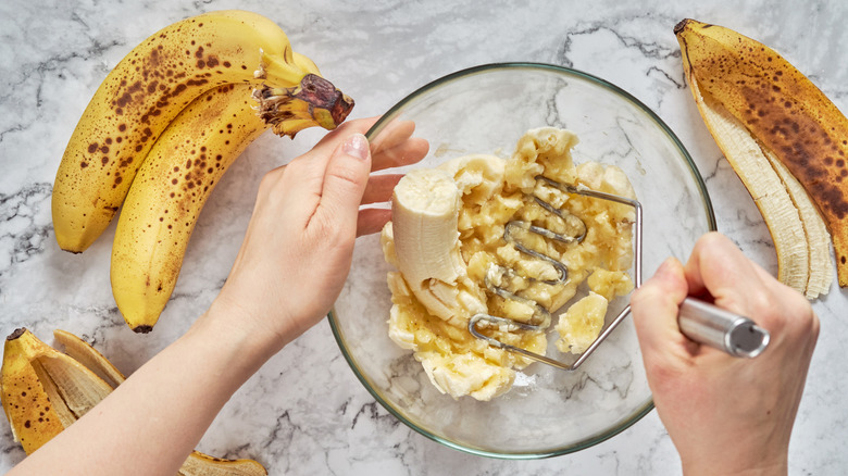 Person mashing ripe bananas in large glass bowl