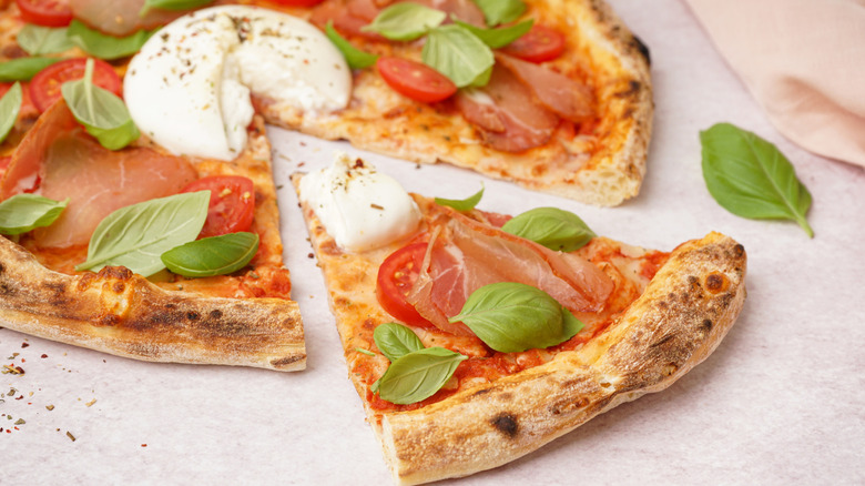 A thin-crust pizza topped with burrata, basil, and sliced ham