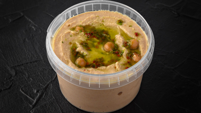 Plastic container of store-bought hummus with olive oil and chick peas