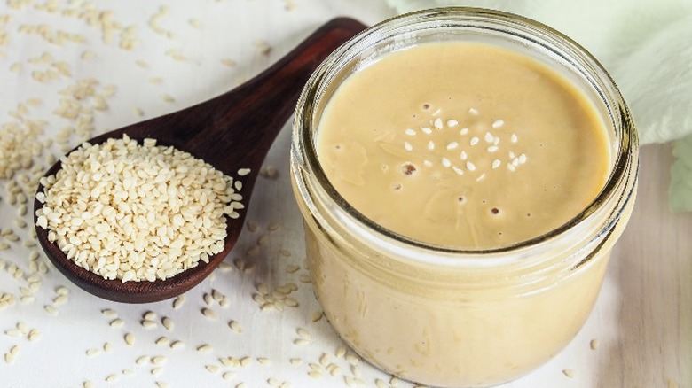 A spoonful of white sesame seeds next to a jar of tahini.