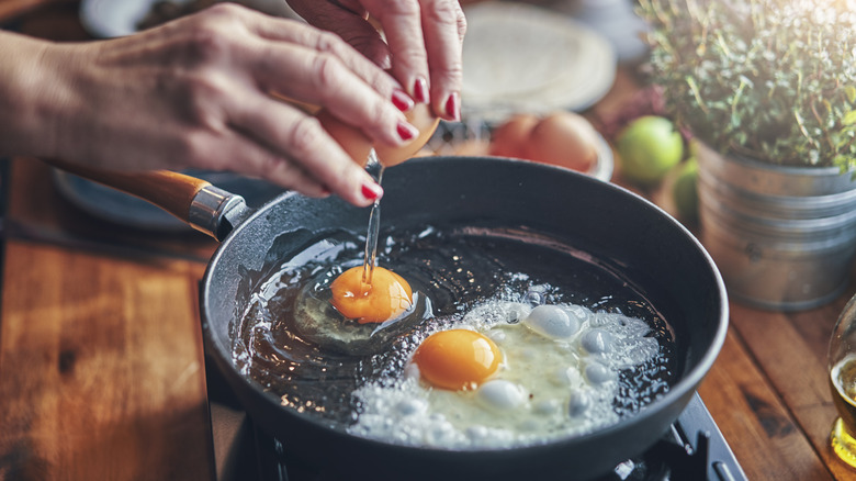 A woman cracks eggs into a frying pan