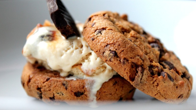 Two thick chocolate chip cookies with a scoop of melting vanilla ice cream