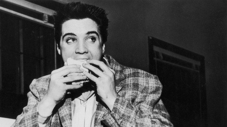 Black and white photo of Elvis Presley taking a bite of a sandwich or pastry