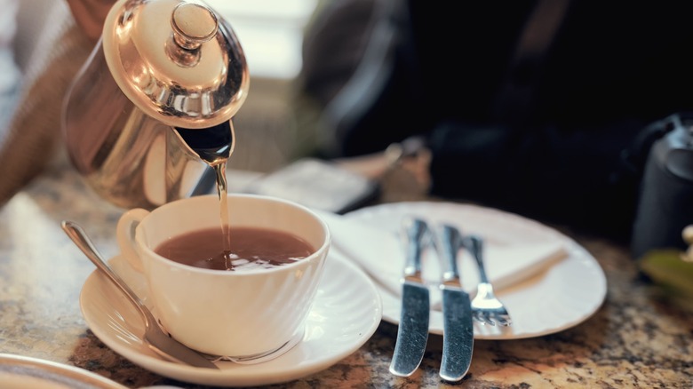 A cup of tea being poured from a metal pot