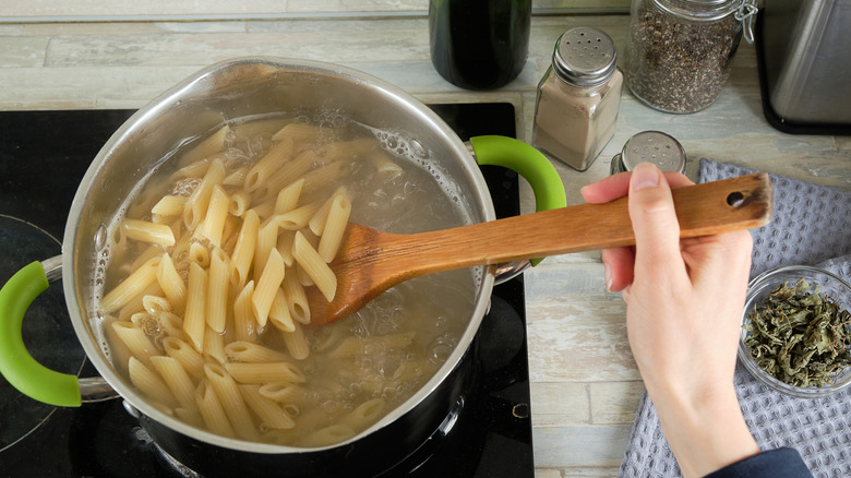 Penne pasta being stirred in a pot with a wooden spoon