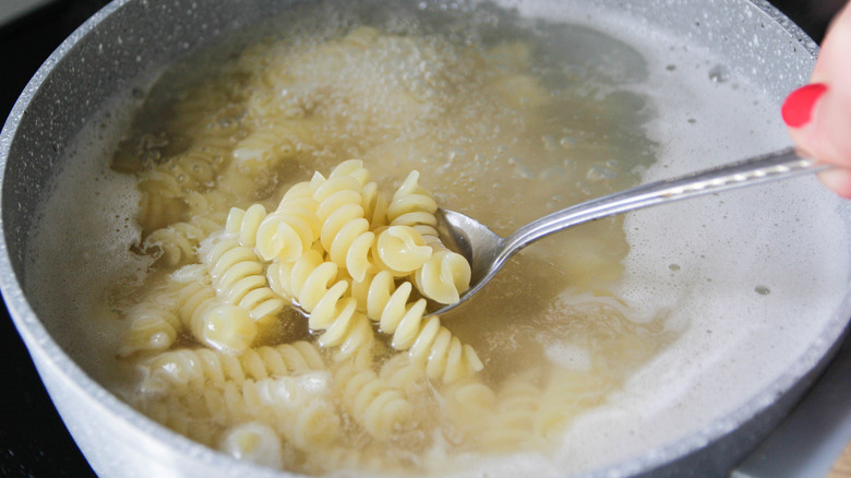 A person stirring pasta in a pot full of boiling water