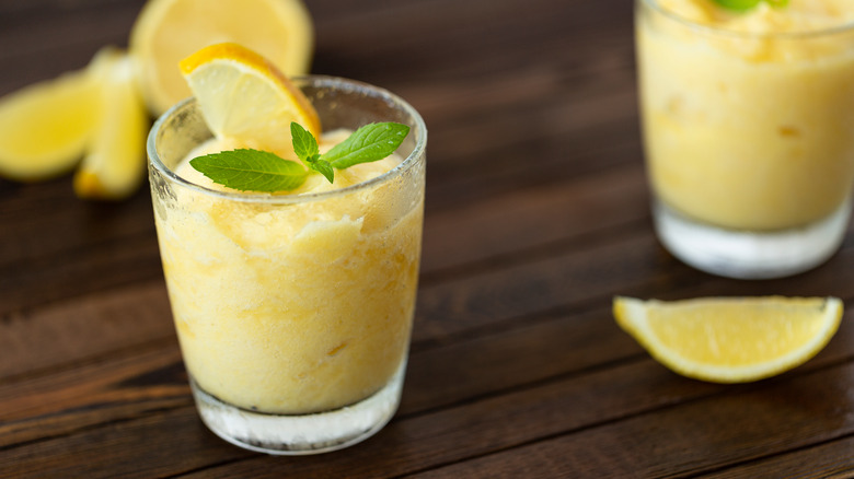 lemon slush drink on wooden table with lemon slice and mint garnish