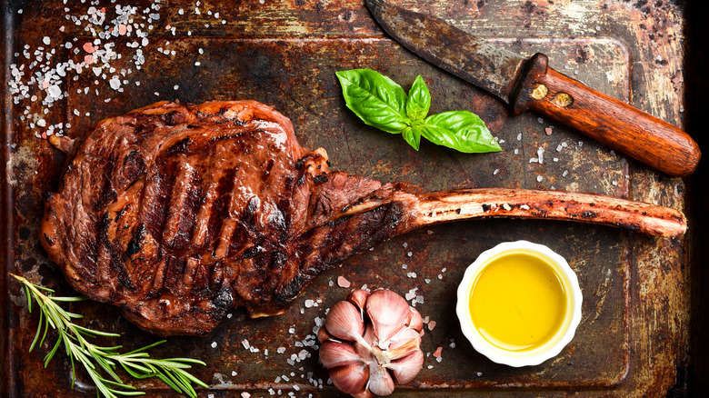 grilled tomahawk steak with sauce, seasonings, and a rusty knife