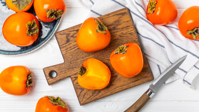 Pile of persimmons on wooden board and plate with knife