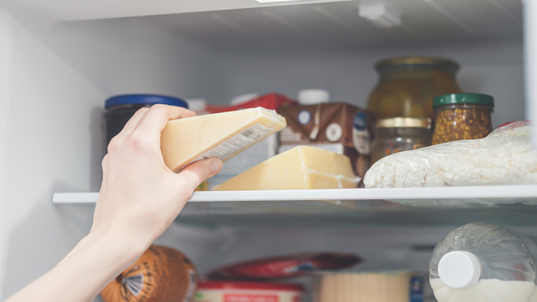 A person's hand putting an unopened sealed wedge of hard cheese in the fridge