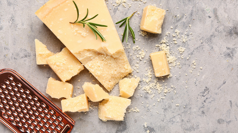 A wedge of parmesan cheese with smaller chunks and a microplane