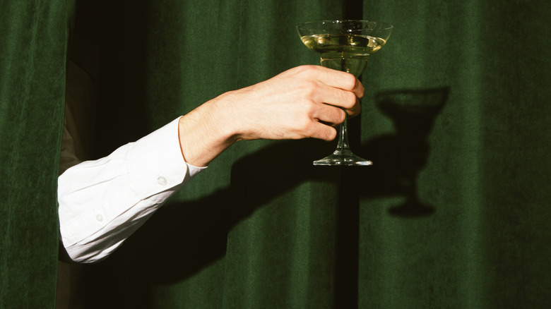 Hand with martini glass sticking out from green curtain