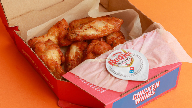 Chicken wings in a Domino's box with tub of hot sauce