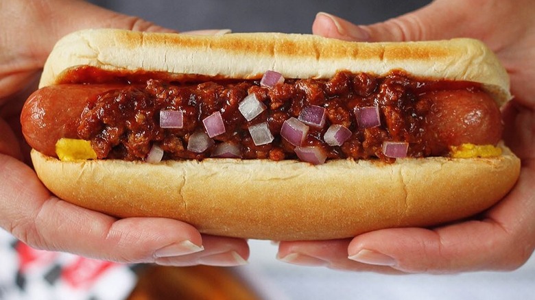 Hands holding chili dog with red onions