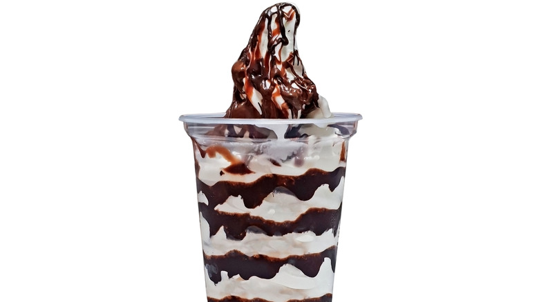 Vanilla soft serve with chocolate sauce in a clear plastic cup